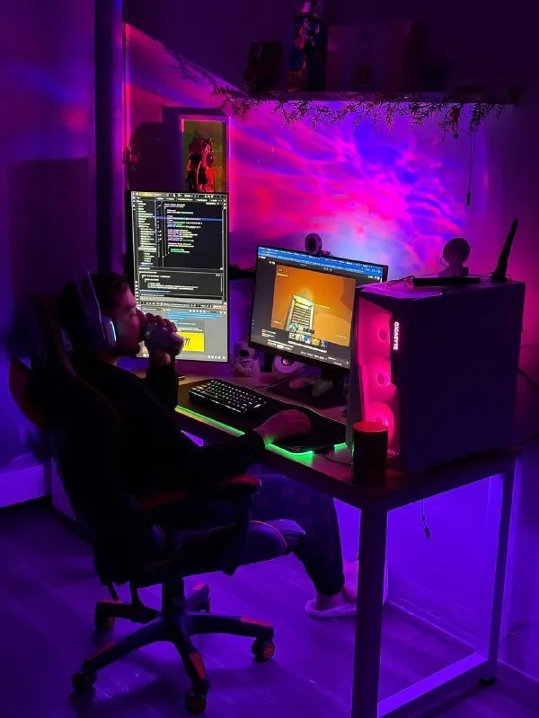 Maks at his desk, lit in purple and pink, with code on the screen